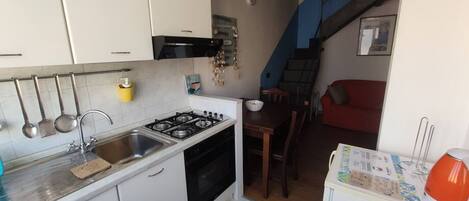 A compact kitchen with white cabinets, a gas stove, and a sink. There's a dining area with a wooden table and chairs, and a red sofa in the background.