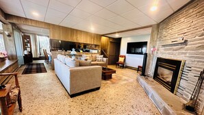 Amplia sala de estar con sofá, mesa de centro y chimenea. Se ve una cocina al fondo.