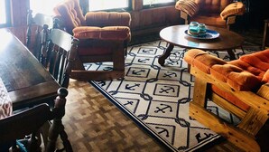 Interior acogedor de una cabaña con paredes de madera, una mesa de comedor, dos sillones y una mesa baja.