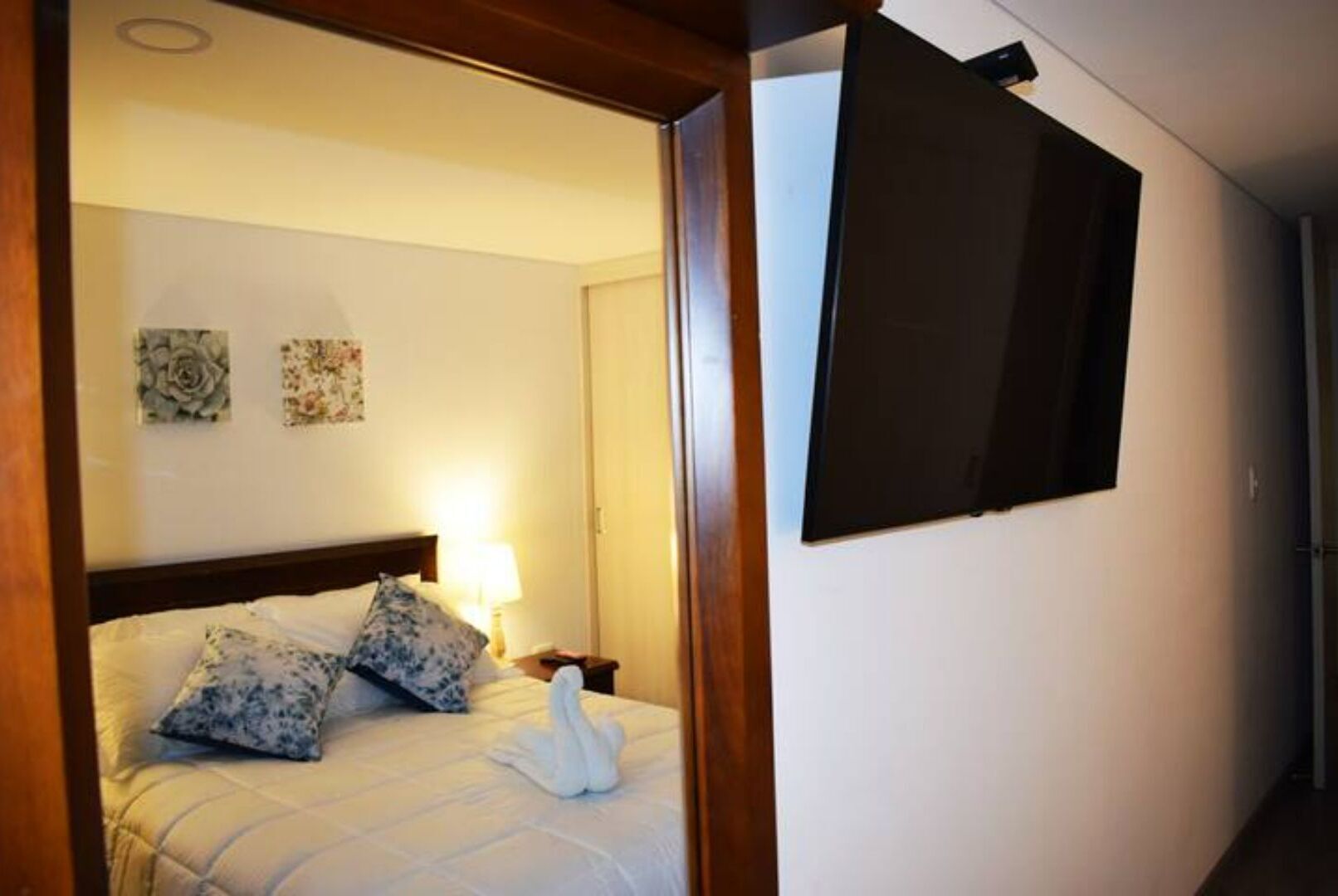 A hotel room with a bed, a nightstand, a lamp, and a wall-mounted TV.