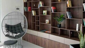 A modern living room with a large wooden bookshelf filled with books and decorative items, a round wire chair with cushions, and a potted plant. - Apartamento Familiar de Lujo al Lado del Lago (Paipa)