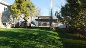 Un jardin avec une pelouse, une terrasse en bois, une aire de jeux et une maison.
