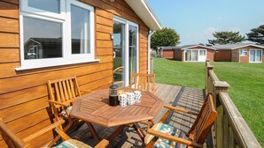 Ein Holzhaus mit einer Terrassenfläche, die Tisch und Stühle, eine Holzterrasse und einen Blick auf benachbarte Häuser bietet.