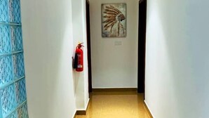 Un couloir avec un extincteur fixé au mur, un sol carrelé et un tableau accroché au mur.