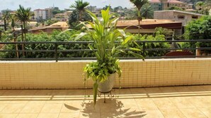 Un balcon agrémenté d’un pot de fleurs, un sol carrelé et une vue sur un paysage urbain avec des immeubles et des palmiers.