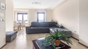 A modern living room with a grey sectional sofa, a coffee table with a plant, and a dining area with a table and chairs.
