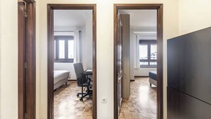 A hallway leading to a bedroom with a bed, a desk, and a chair.