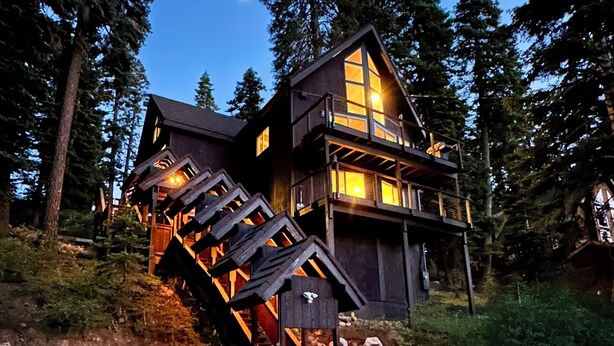 A two-story wooden cabin with a stone foundation, surrounded by trees, and featuring a staircase leading to the upper level. - Tahoe Treetop Escape 4BR Near Trails & Donner Lake (Truckee,)