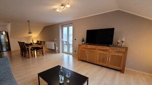 A spacious living room with a dining area, a flat-screen TV, and a large window.