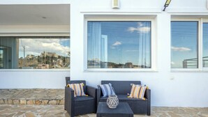 An outdoor seating area with a stone floor, two dark wicker sofas with striped cushions, and a small table with a decorative vase. - Aegean Blue Apartment (Ligaria)