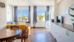 A modern kitchen with a dining area, large windows with curtains, a view of the landscape, and a TV on the counter. - Aegean Blue Apartment (Ligaria)