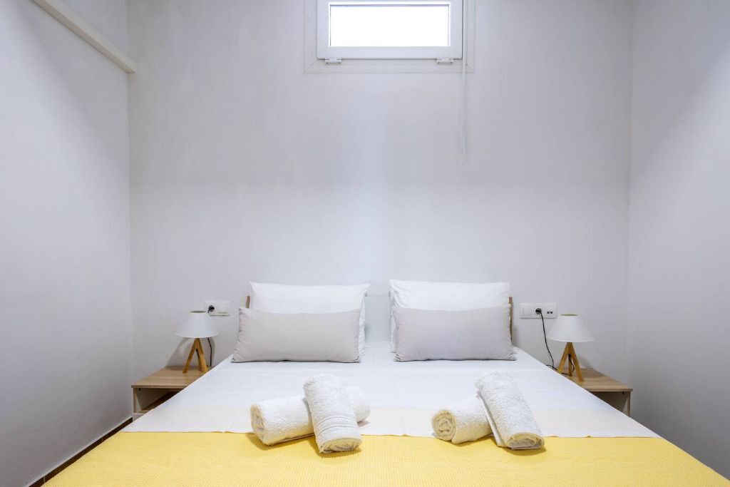 Una camera d'albergo con un letto, due comodini, una finestra e una coperta gialla.