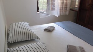 Una cama individual con almohadas a rayas, una toalla doblada y una ventana con cortinas de encaje.
