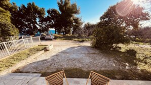 Un patio al aire libre con una mesa de mármol y sillas de mimbre, rodeado de grava y árboles.
