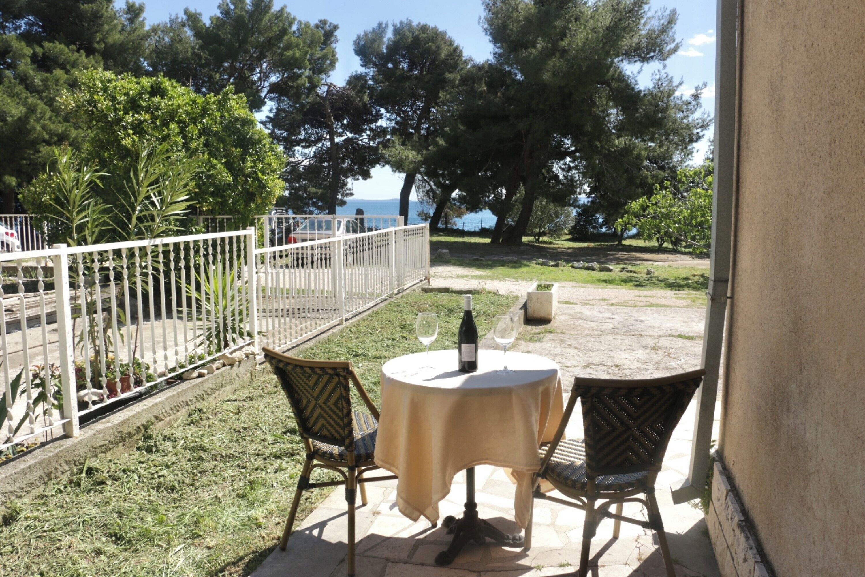 An outdoor patio with two round tables, each with a wine bottle and glass, surrounded by wicker chairs.