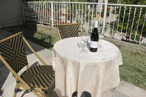 Una mesa redonda con mantel blanco, dos sillas, una botella de vino y una copa sobre la mesa.