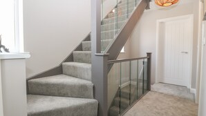 A staircase with carpeted steps, a glass railing, and a pendant light.