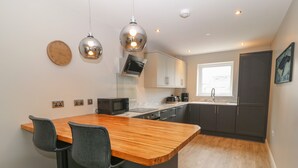 A modern kitchen with a wooden island, bar stools, a microwave, and dark cabinets.