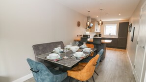 A modern dining area with a marble table, blue and orange chairs, and a kitchen in the background.