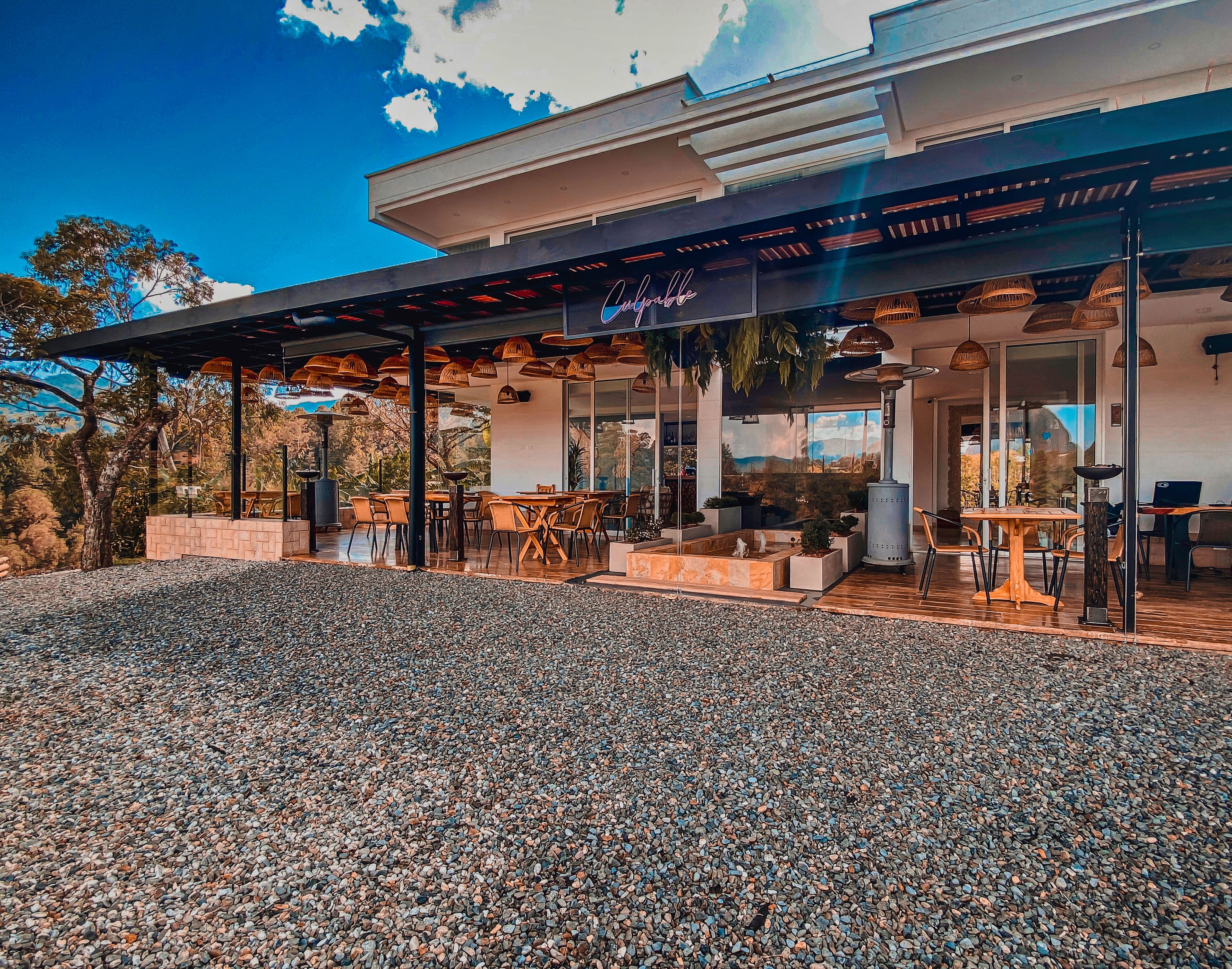 A modern outdoor dining area with tables and chairs, a pergola, and a view of the surrounding landscape.