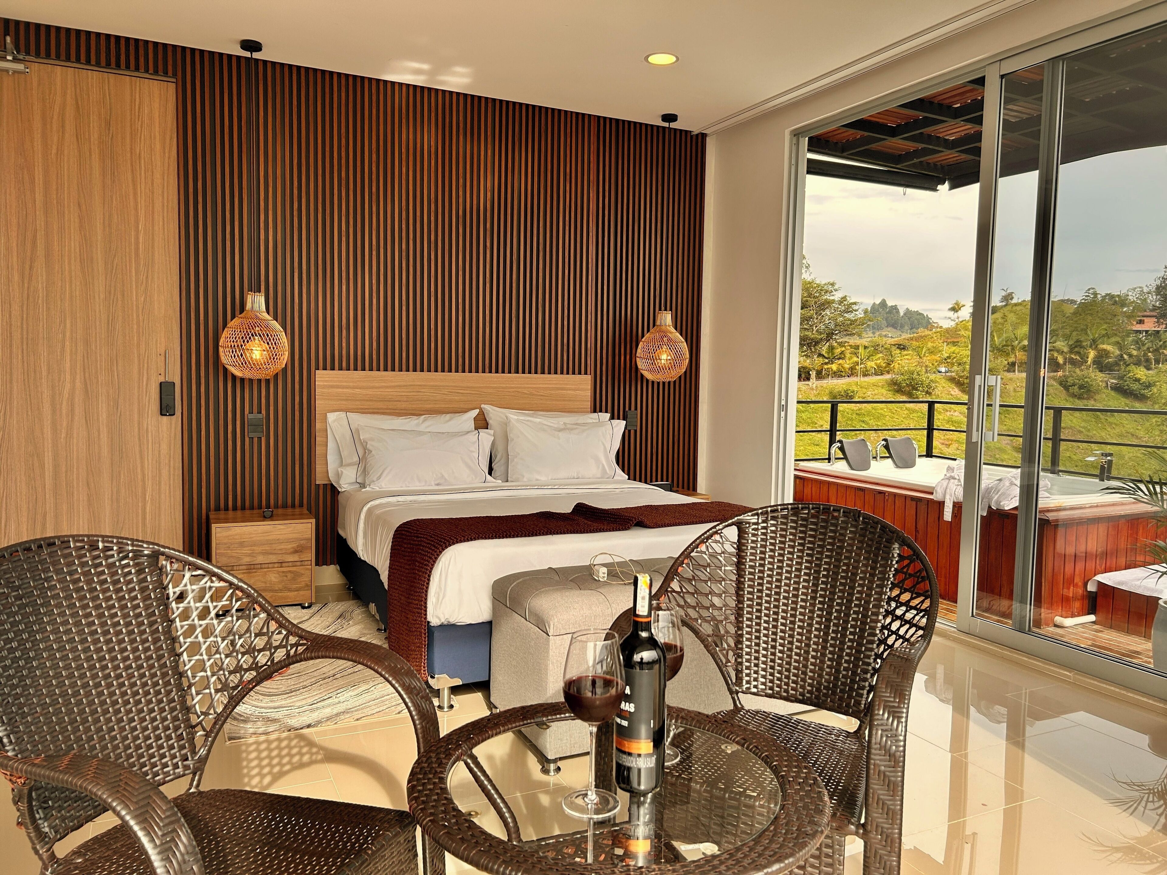 A modern bedroom with a large bed, two wicker chairs, a small table, and a balcony with a hot tub.
