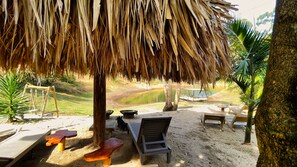 Zona de playa con una estructura de techo de paja, bancos de madera y vista a una masa de agua tranquila con un bote.