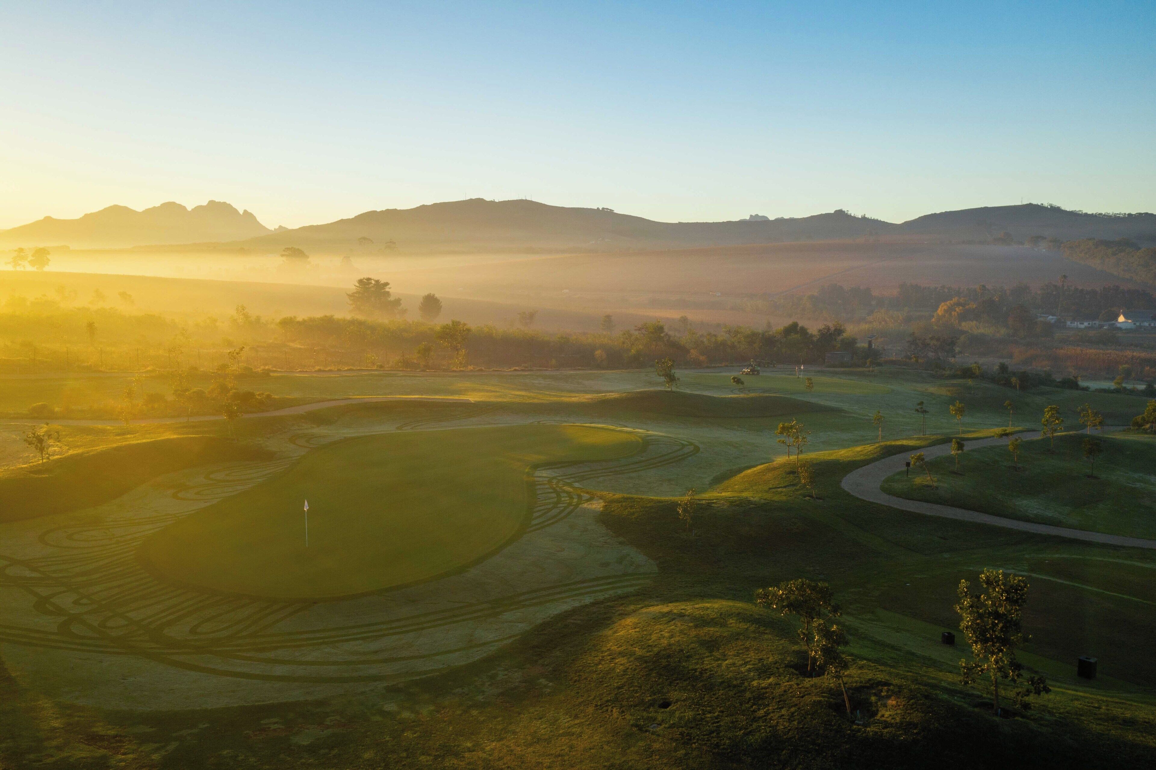 A golf course with multiple holes, a flag, and a distant mountain range.