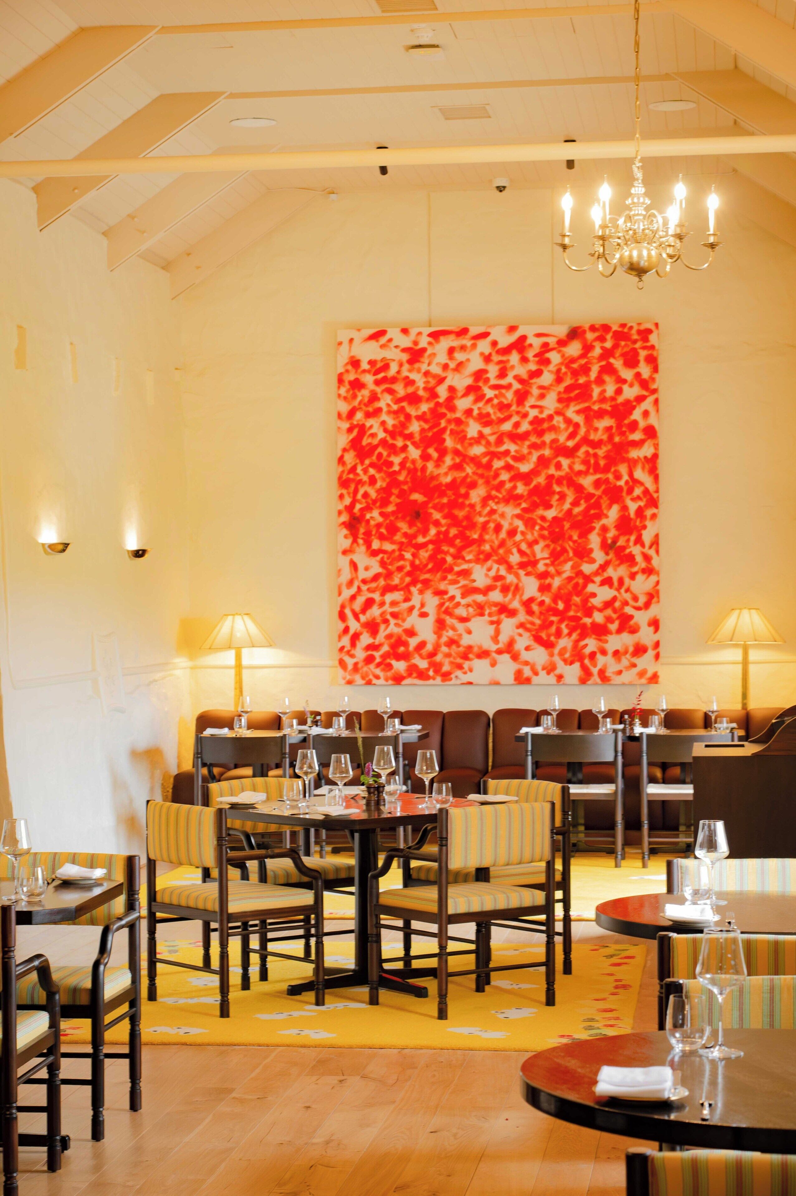 Interno di un ristorante con soffitti alti, lampadari e un'ampia opera d'arte astratta nei toni del rosso e del bianco.