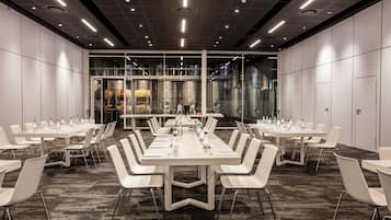 A conference room with multiple tables and chairs, a carpeted floor, and a glass wall with industrial elements.