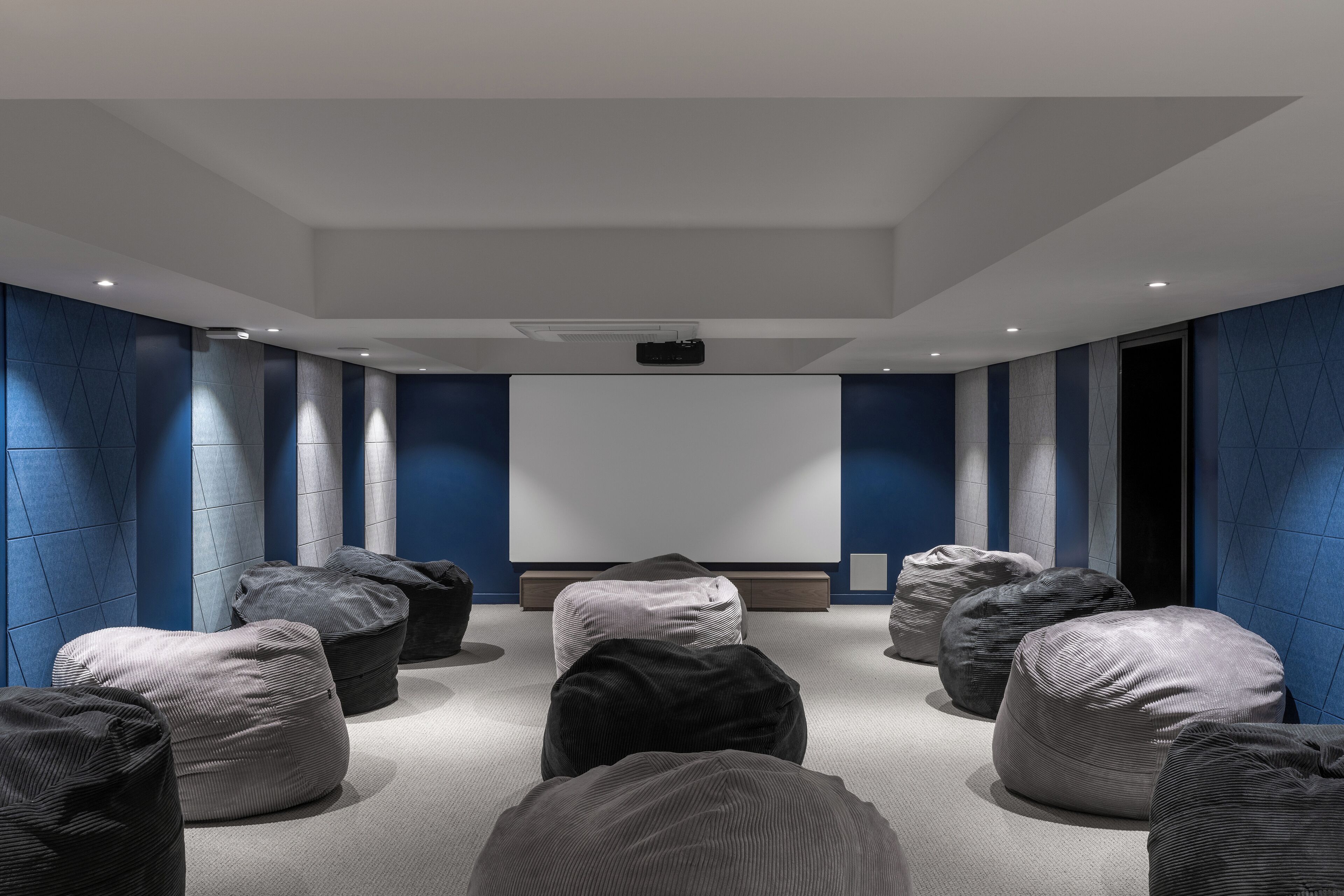 A modern conference room with a large screen, multiple seating areas, and a neutral color scheme.