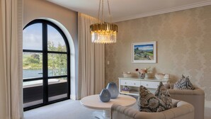 A room with a large arched window, a round table, a sofa, a chandelier, and a painting on the wall. - The Hazendal Hotel and Spa (Stellenbosch)