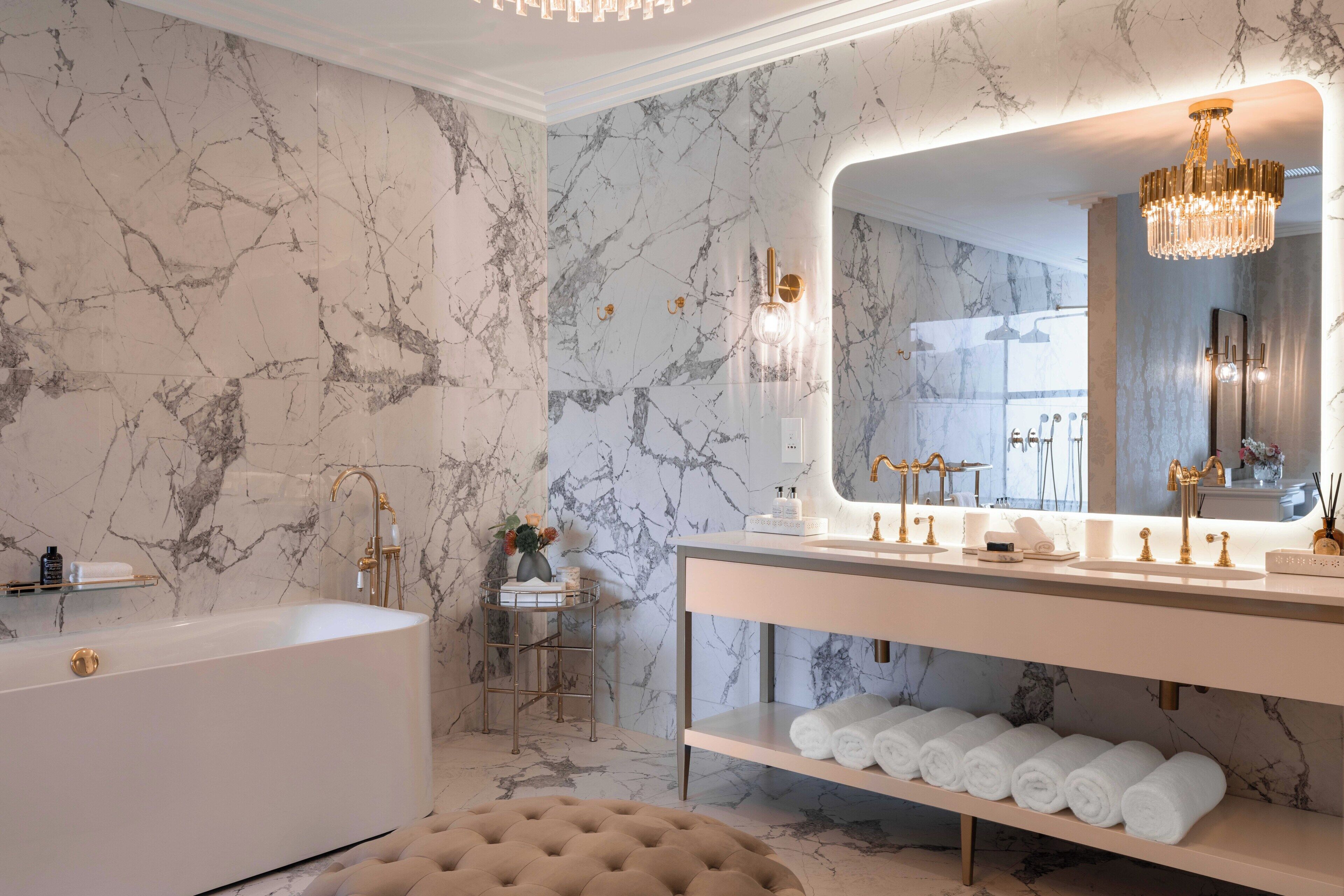 Un bagno con parete in marmo, una vasca, un mobile lavabo con specchio e un lampadario.