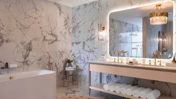 Un bagno con parete in marmo, una vasca, un mobile lavabo con specchio e un lampadario.