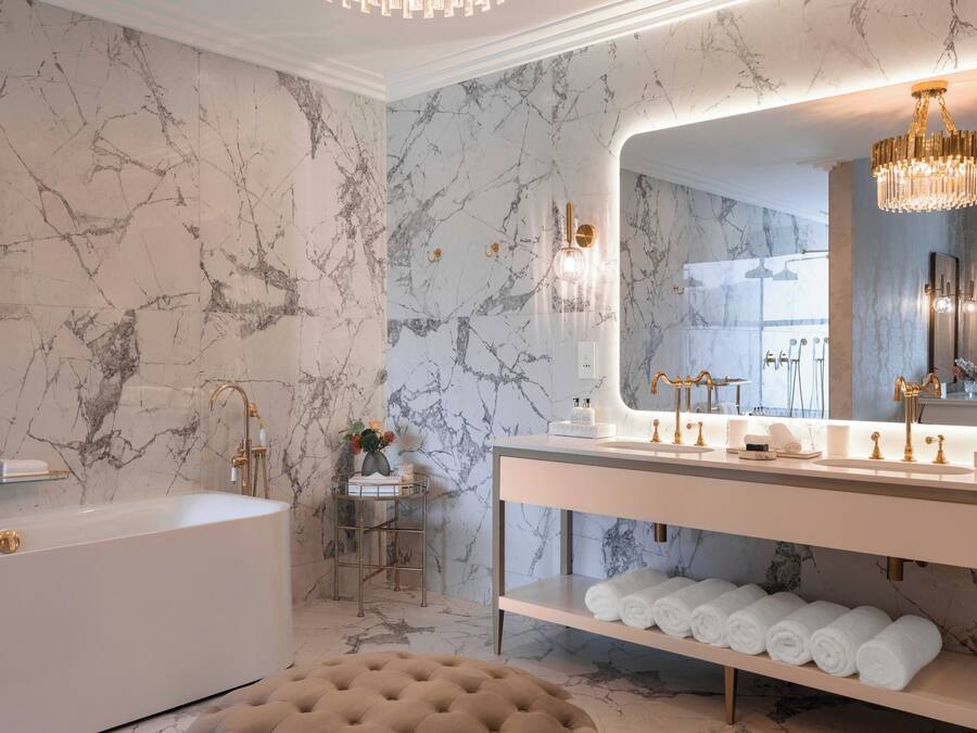 Un bagno con parete in marmo, una vasca, un mobile lavabo con specchio e un lampadario.