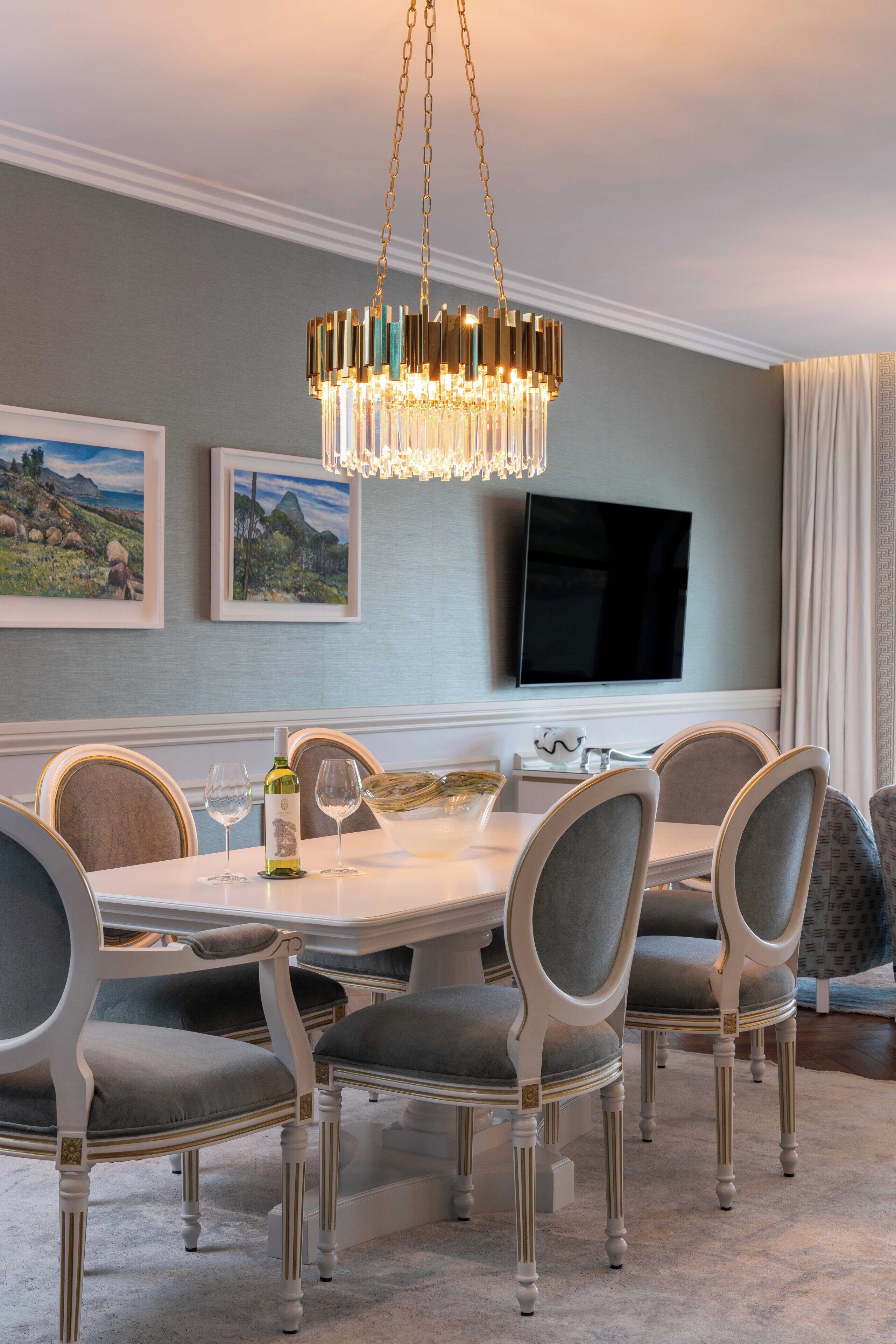 A dining room with a chandelier, a television mounted on the wall, and a table set for four.