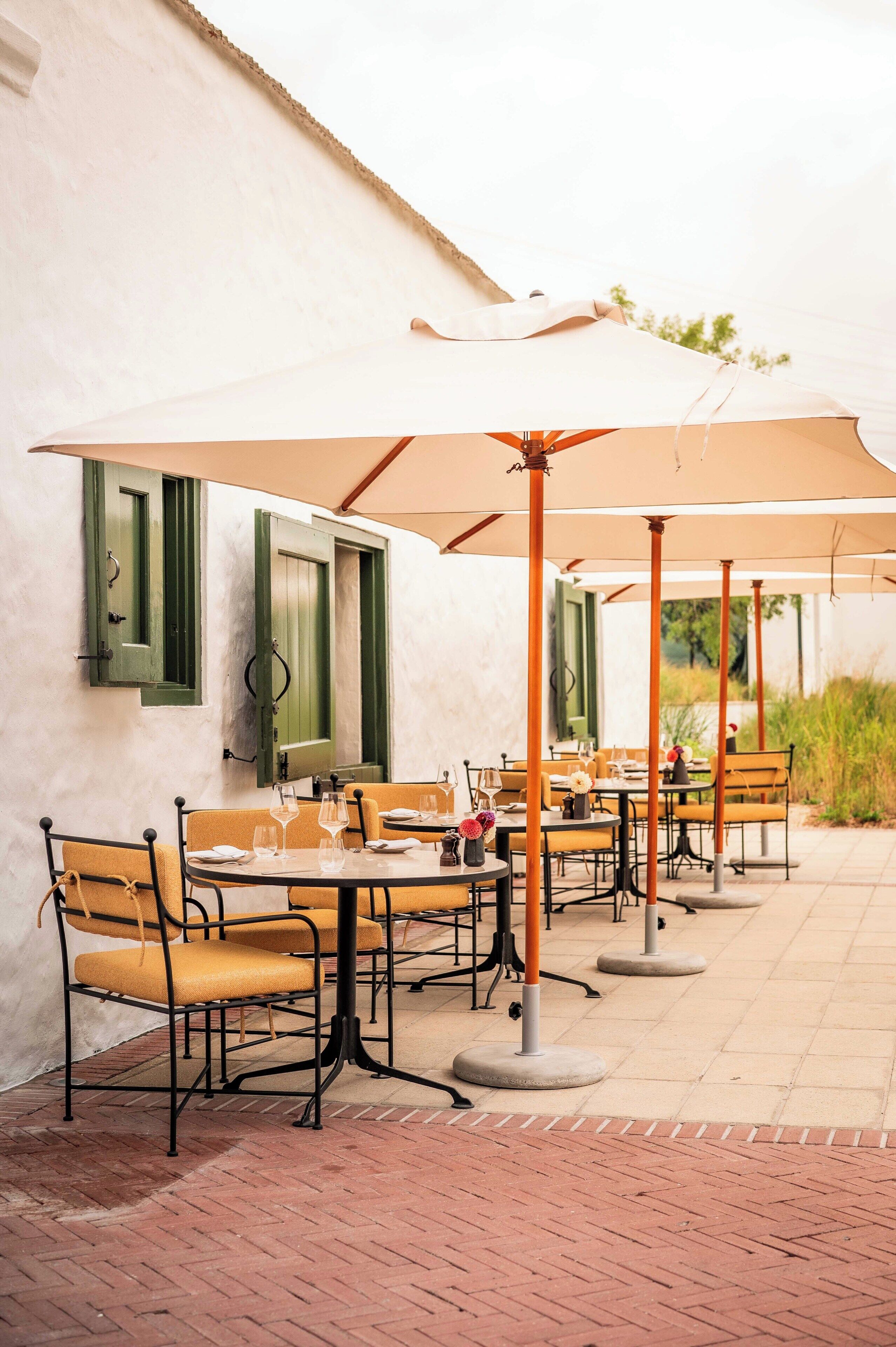 An outdoor dining area with tables and chairs, umbrellas, and a brick floor.