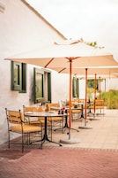 Un área de comedor al aire libre con mesas, sillas, sombrillas y piso de ladrillo.
