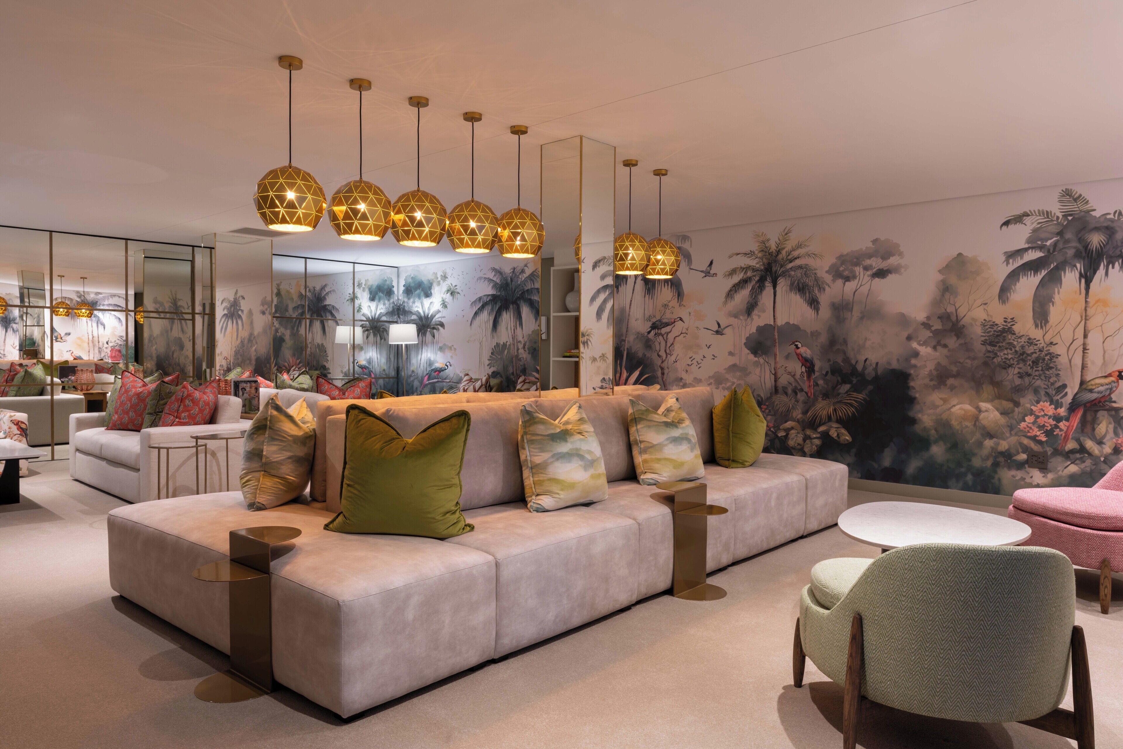 Un salon moderne avec un canapé, des fauteuils et une table basse. On y trouve des lampes décoratives et une fresque murale.