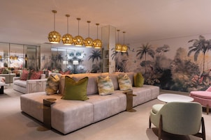 Una sala de estar moderna con un sofá, sillones y una mesita de centro. Hay lámparas decorativas y un mural en la pared.