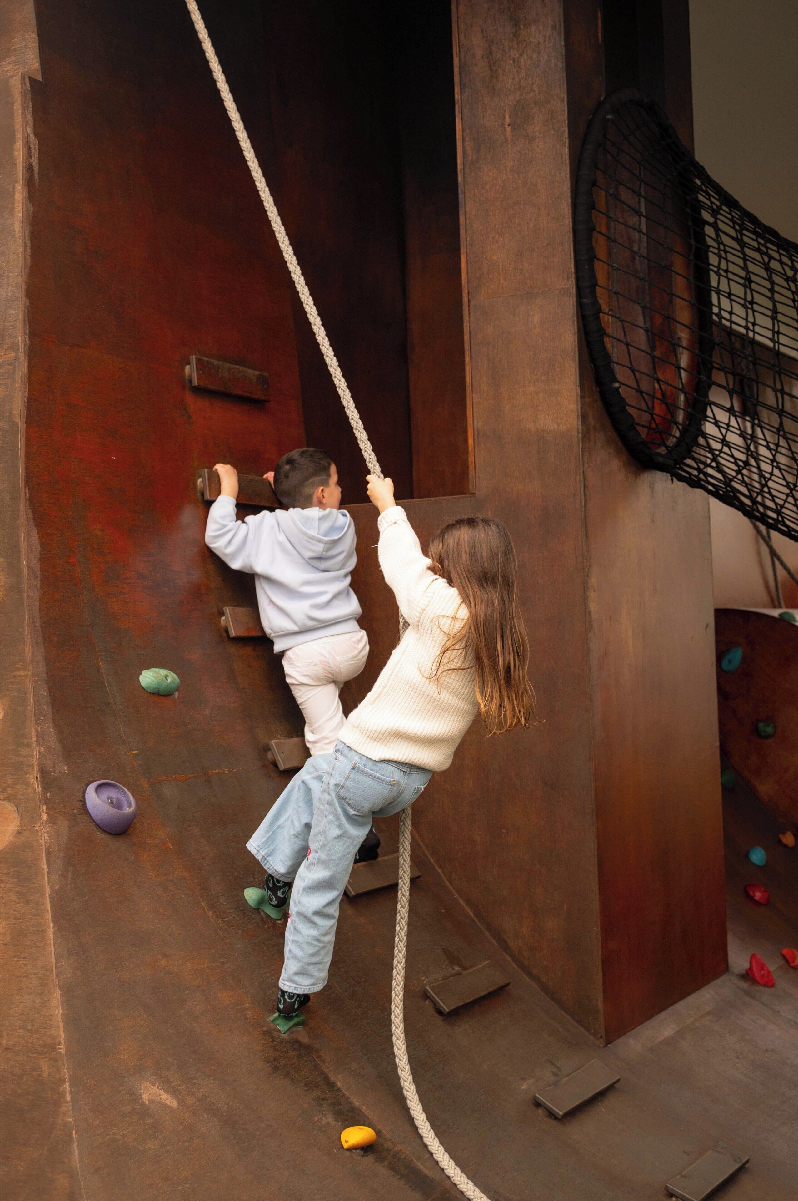 Dos niños escalando una pared de madera con diferentes puntos de agarre.