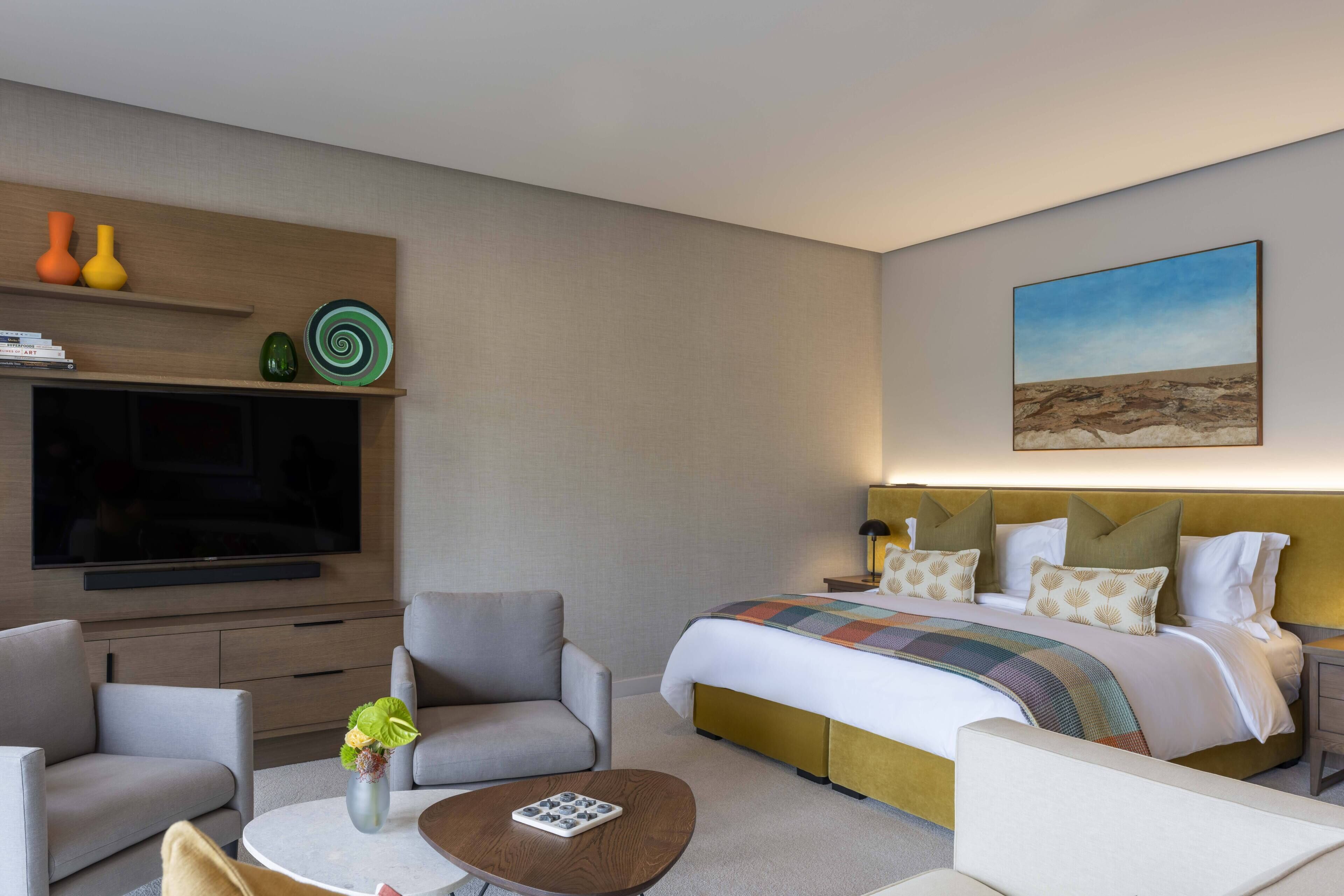 A hotel room with a bed, a TV, a sofa, a coffee table, and a painting on the wall.
