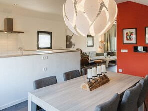 A modern kitchen with white cabinetry, a built-in island, and a dining area with a wooden table and four chairs. - Luxurious Holiday Home With Rural Character (Ruinerwold)