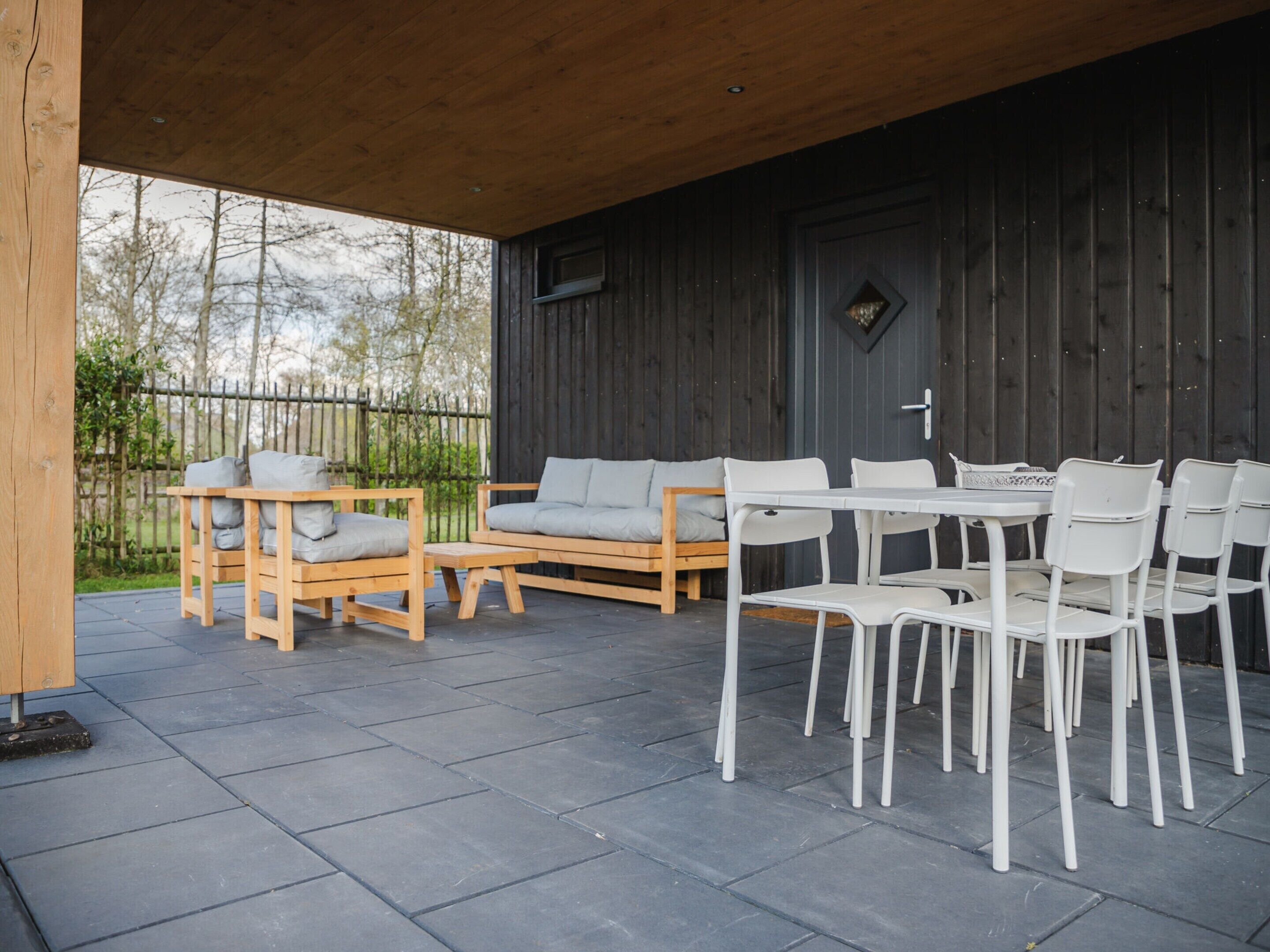 An outdoor patio area with wooden furniture, including a sofa and chairs, and a table.