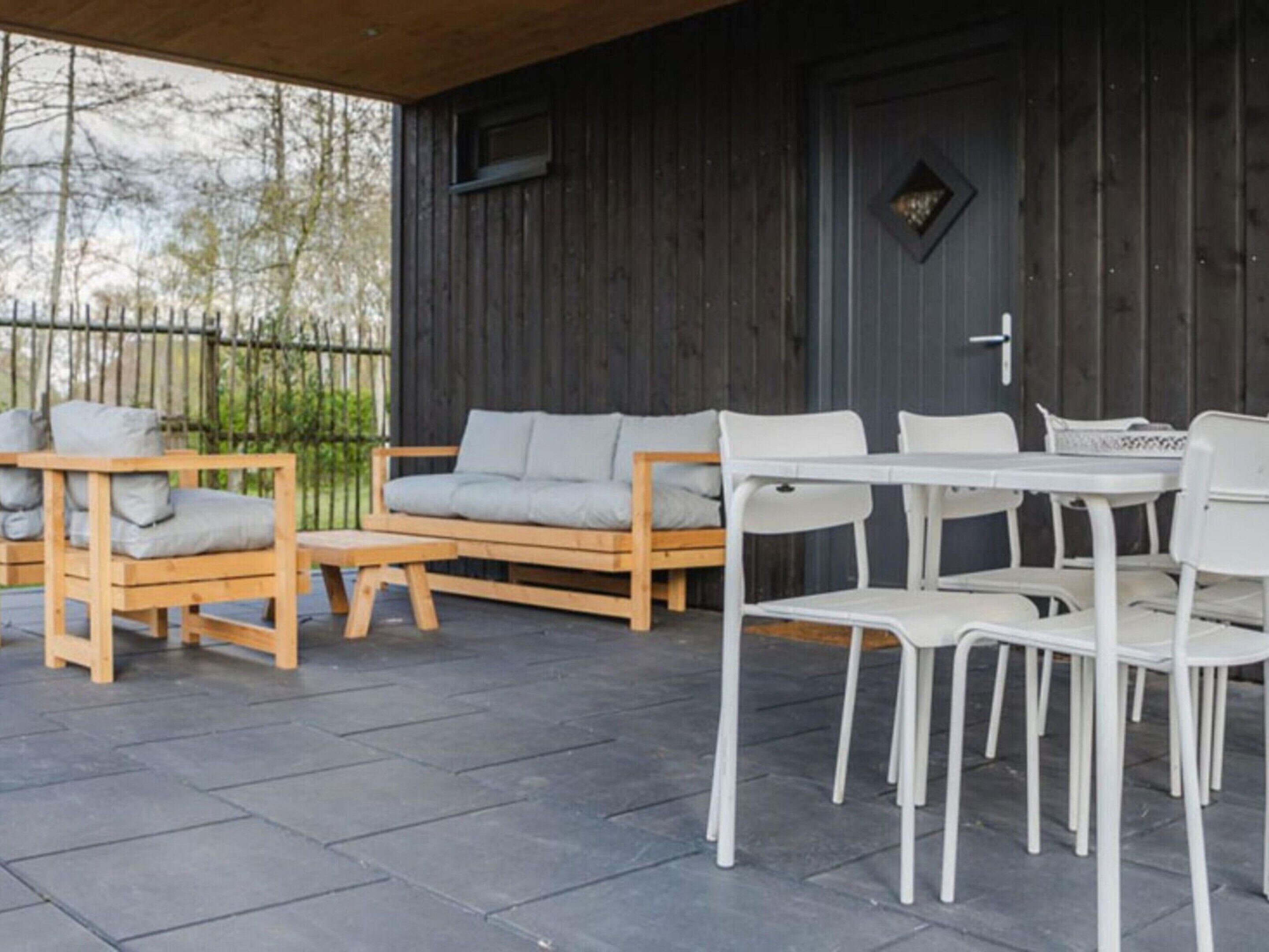 An outdoor patio area with a wooden sofa, white chairs, and a table.