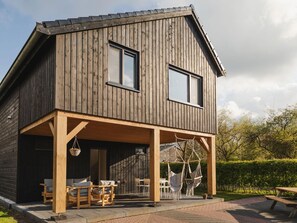 A wooden house with a covered porch, outdoor seating, and a view of the surrounding greenery. - Luxurious Holiday Home With Rural Character (Ruinerwold)