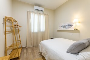 A bedroom with a bed, a wooden drying rack, a window with curtains, an air conditioner, and a wall-mounted lamp. - Casa Abuela Toña by Huskalia | city center (Los Llanos de Aridane)