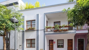 A two-story building with a balcony on the upper floor, a wooden door, and a small porch area.