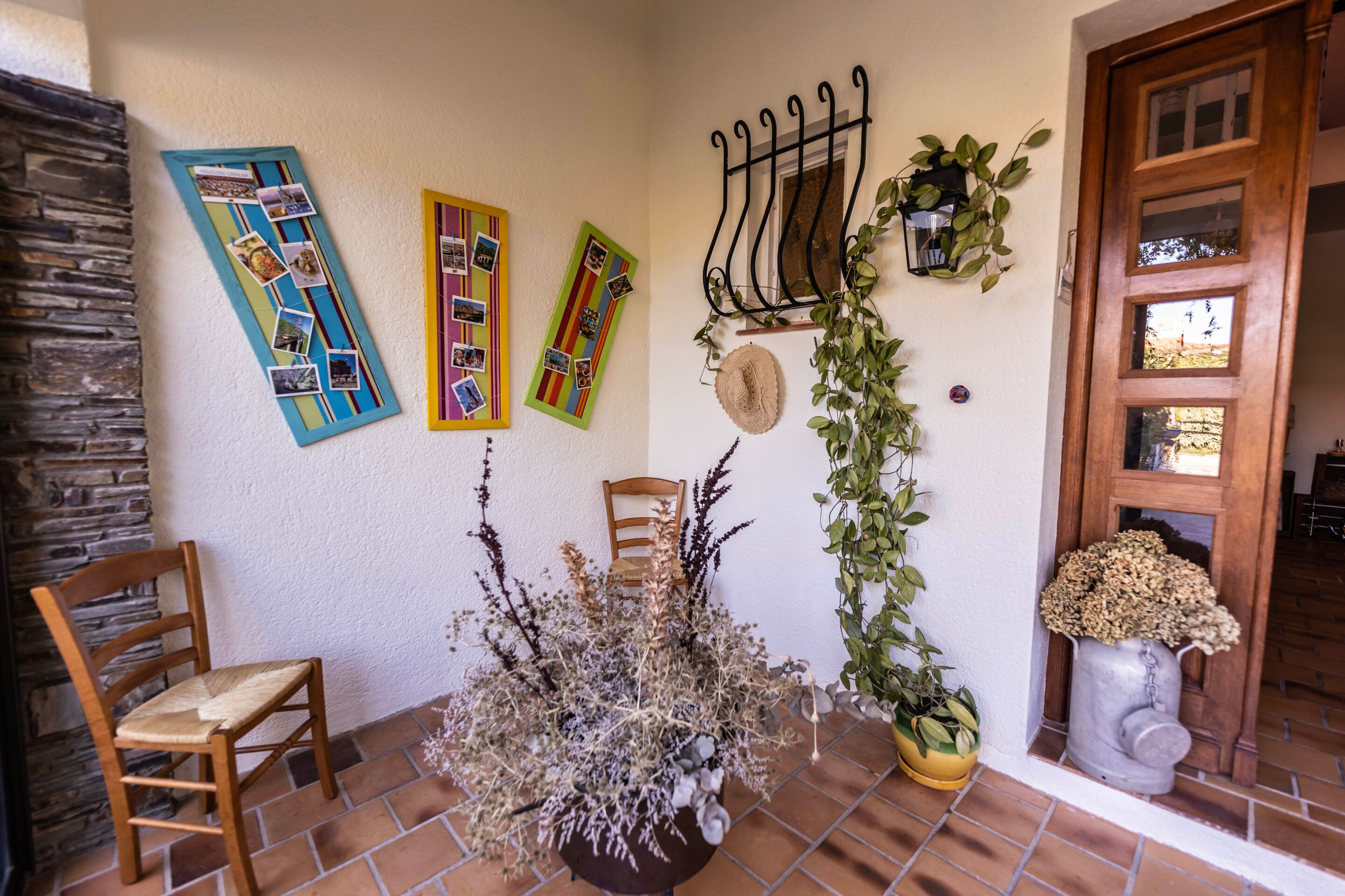 A patio area with a wooden chair, a potted plant, and a wall decorated with photos and a metal rack.
