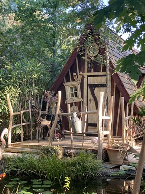 A rustic wooden cabin with a sloped roof, surrounded by lush greenery and a small pond with lily pads. - Mas Del Flor (Villelongue-dels-Monts)