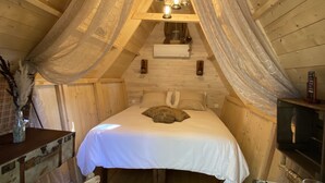 Un dormitorio abrigado en el ático con cama, una silla, una mesita y techo de madera.